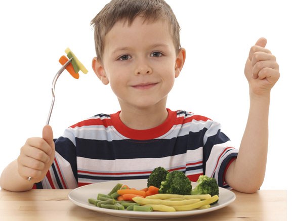 A smiling child giving a thumbs up over a plate of fresh vegetables